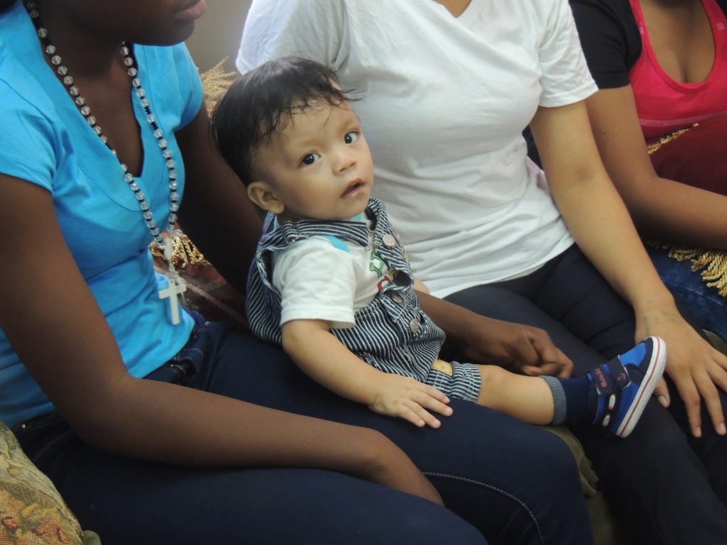 Jason, the son of one of the residents at the Together in Peace safe house in Guyana, sits with two women.