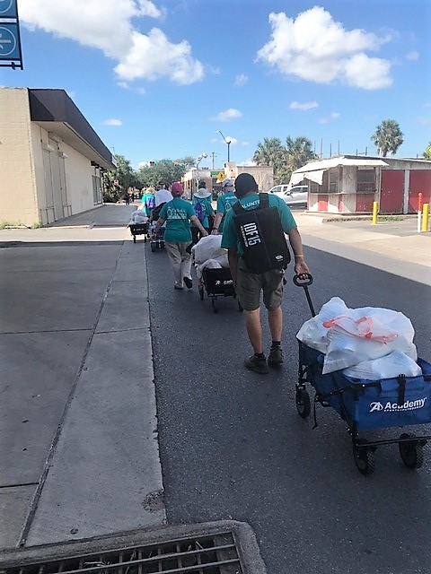 Voluntarias y voluntarios de Caridades Católicas empujan carretas llenas de suministros hacia el puente que va a México, donde los distribuirán a inmigrantes del otro lado.