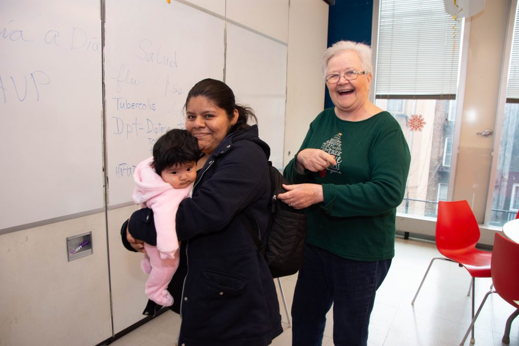 CAPTION: Sharing a happy moment at LSA Family Health Service, where Sister Suzanne teaches classes like Día a Día con Tu Bebé (“Day by Day with Your Baby”). Before she “retired” five years ago and became a volunteer, Sister Suzanne climbed countless flights of stairs in East Harlem tenements for more than 20 years, helping new mothers care for their infants. A Sister of Mercy who ministered in Nicaragua with Maryknoll nuns for 13 years, Sister Suzanne returned home in 1993 to care for her father and to find a job working with Latin American immigrants. A friend told her about LSA, and she has been here ever since. (Catherine Walsh photo)