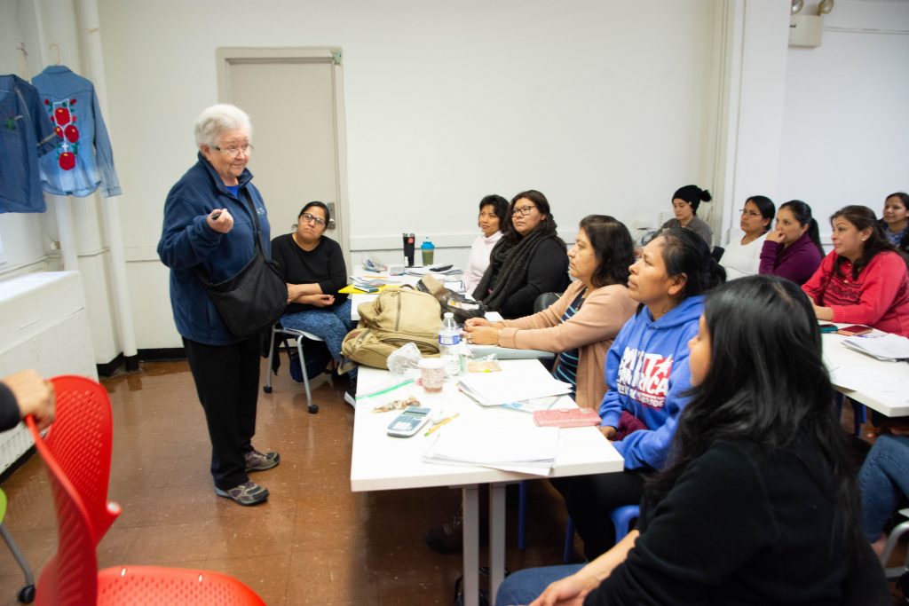 CAPTION: Sister Suzanne chats with CREA students studying for their high-school equivalency exam. She saw the need for the adult learning center upon encountering two women in tears who had been asked to leave an English-as-a-second language (ESL) class. “They weren’t literate in Spanish and couldn’t keep up,” she said. Many CREA students speak an indigenous language as a first language; some have never been to school before and come to CREA to learn basic Spanish literacy, as well as to take ESL classes. The center is offering some online classes during the pandemic. (Catherine Walsh photo)