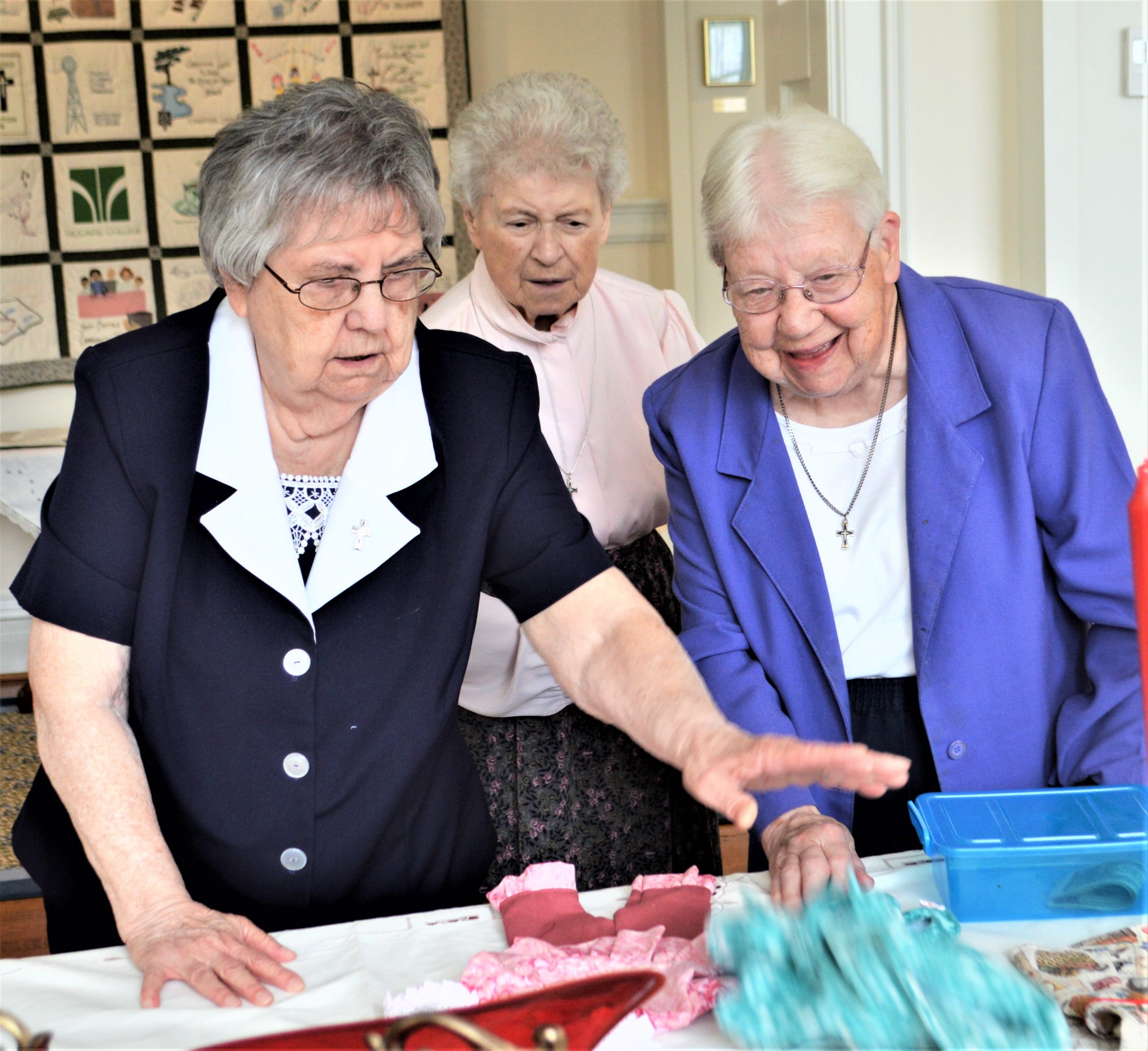 Sister Bernadette Geiser, left, shows Sisters Mary Priscilla Faltisko, center, and M. Norine Truax items to be raffled. Proceeds from the project are going to benefit migrants at the U.S. border with Mexico.